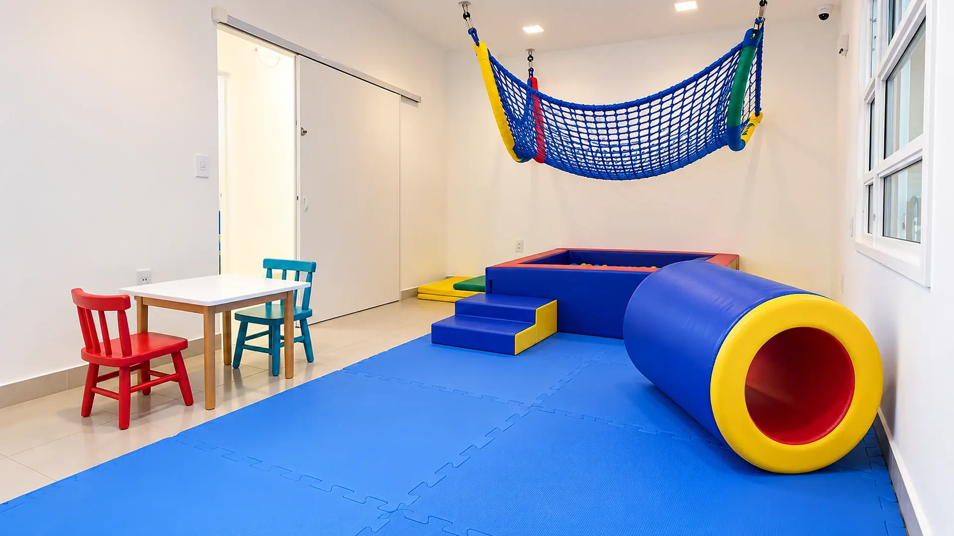Sala de psicomotricidade da Help!, com tatame azul, rede suspensa, piscina de bolinhas e mesinha infantil